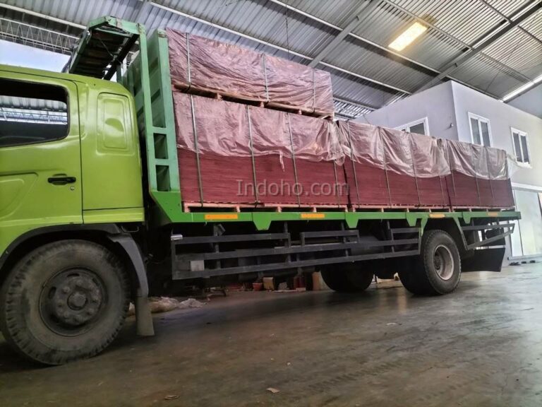 Truk besar bermuatan tumpukan Triplek Phenolic Film Face untuk pengiriman material bekisting cor beton proyek konstruksi.